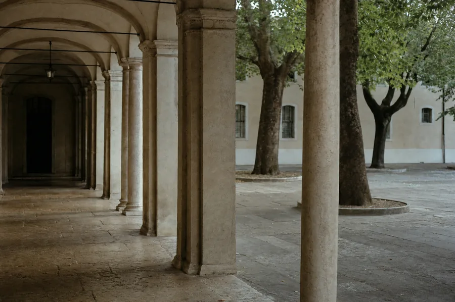 Il portico e il cortile alberato di una scuola, vuoti nel pomeriggio